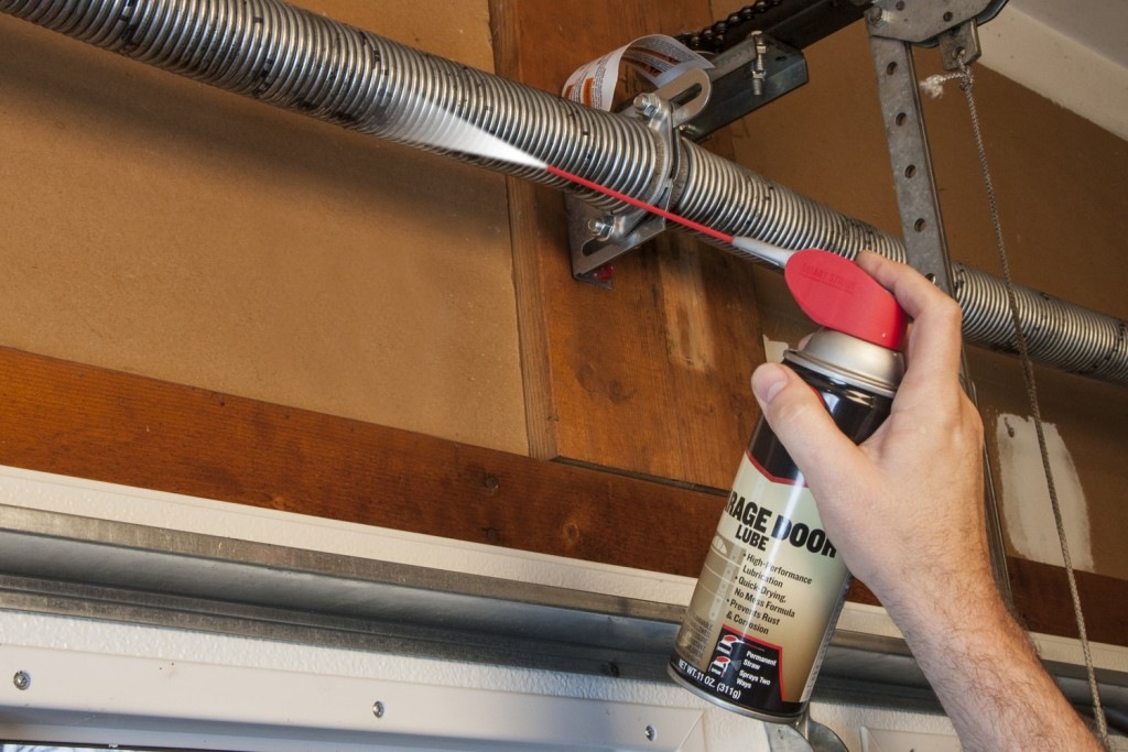 A professional technician is shown lubricating the moving parts of a residential garage door to ensure smooth and quiet operation. Regular maintenance like this helps prevent common issues and prolongs the lifespan of the garage door system